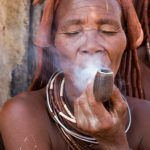 An elderly Himba woman smoking a pipe outside her hut on our Namibia photo tour