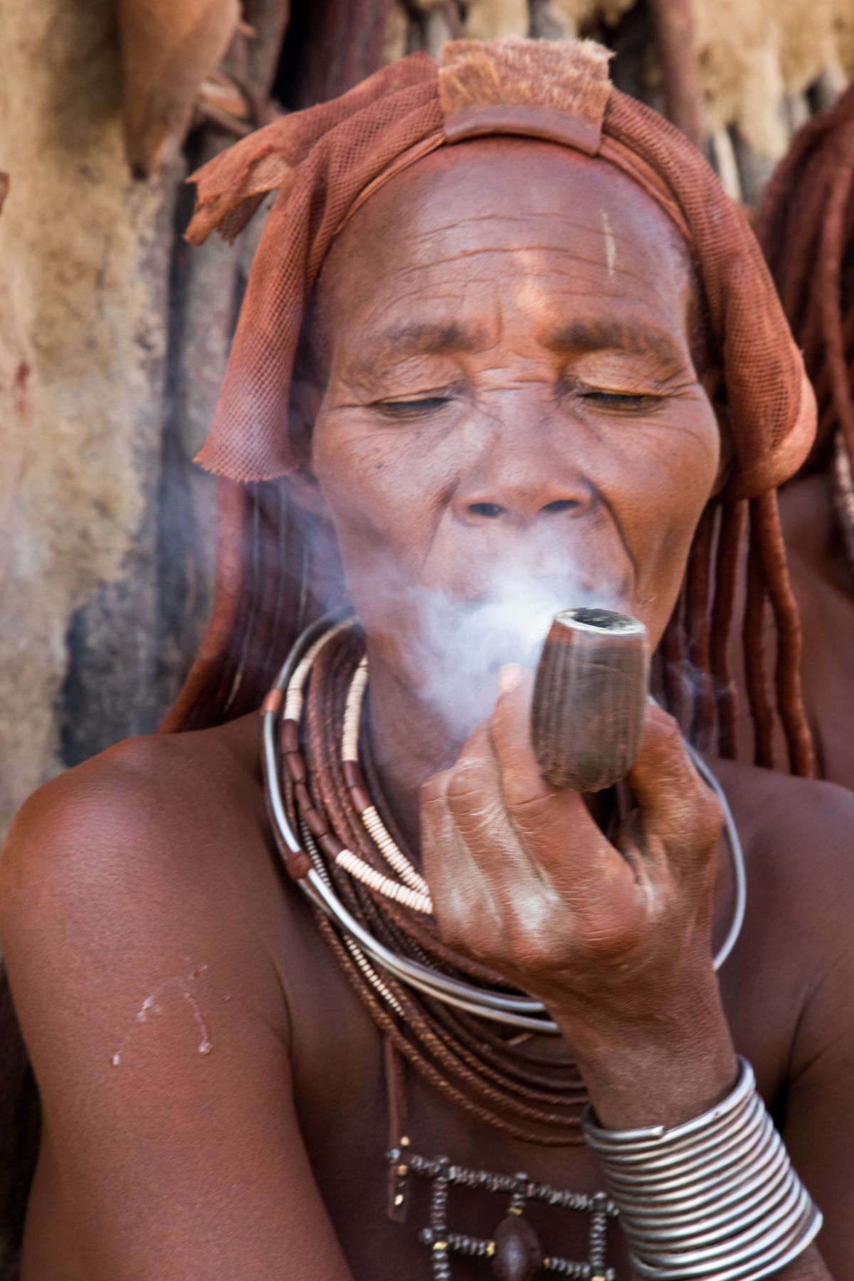 An elderly Himba woman smoking a pipe outside her hut on our Namibia photo tour