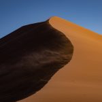 A strong wind blows the sands off the top of Sossusvlei's sand dunes