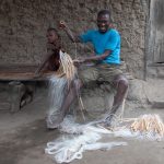 Ajani teaching his daughter how to mend nets in a remote fishing village near the border of Nigeria and Benin on our Benin photo tour