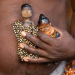 Ancient twin dolls are held by their elderly father during a visit to a Zandro celebration
