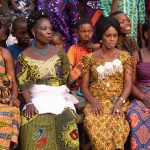 Beninese women sit watching twirling Zangbetos at a ceremony during our photography tour in Benin