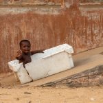 A young child uses a fishing crate to slide down a concrete ramp in one of Benin's coastal fishing villages
