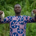 A fisherman holds up two of his caught Tilapia near the border of Benin and Nigeria on our Benin photography tour