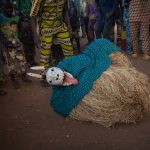 A Guelede mask dancer pretends to pass out in front of onlookers in eastern Benin