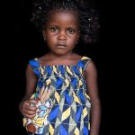 Portrait of a little Sahouie girl named Juliette carrying a doll of her deceased twin sister, Juliana