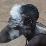 A Voodoo princess sprays white powder on her face to prepare for a dance. White is the highest colour of Voodoo spirituality and represents light