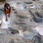 A young girl grinds millet in the grinding pits of her Lotuko village