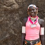 A beautiful young Laarim girl in full decoration preparing for her ceremonial dance. She is standing in front of the granite boulders in her village