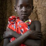 A simply decorated Laarim girl poses for us at the base of a giant wild fig tree in our camp