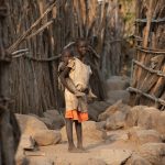 A young Lotuko girl carrying her baby brother through the village on our photo tour of South Sudan
