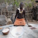 A young Lotuko girl grinds millet in one of the fascinating grinding pits of her village