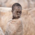 A young Mundari boy pauses in contemplation, looking at his cows
