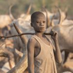 A Mundari boy carrying his stick through camp