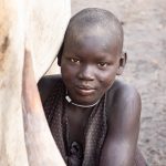 A Mundari girl milks her cow as part of her early morning chores