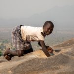 Stella, a young Lotuko girl, grinding dried Okra in the steep hillside grinding pits above her village