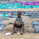 A young boy sits amongst tie-dyed textiles at plant outside Abidjan