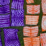 Tie-dyed cloths laid out on grass to dry in the West African sun