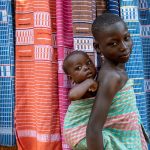 A young girl and her baby sister in front of Korhogo cloth