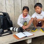 Two Waorani children show their pet Black-headed parrot a book of field notes