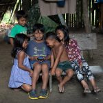 A group of young Waorani children gathered to look at someone's phone