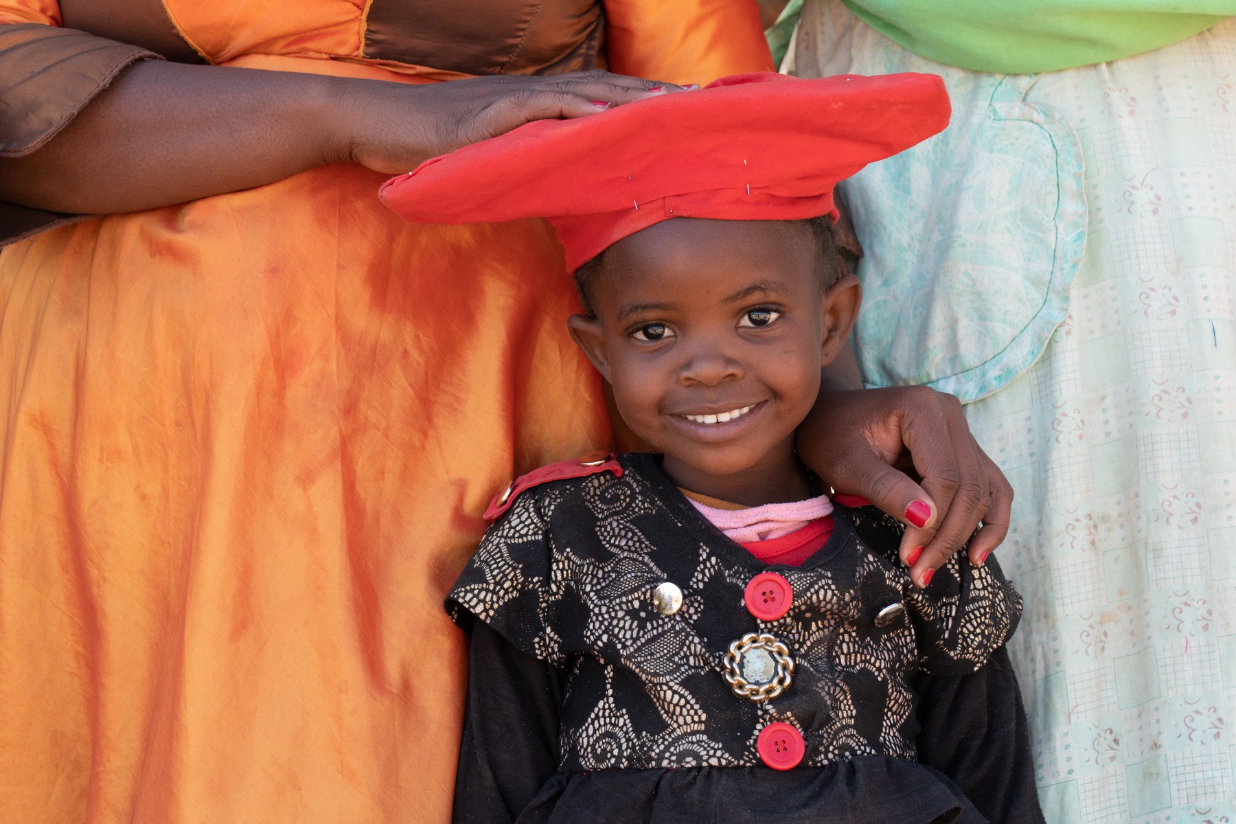 A pretty Herero girl smiles in the protection of her mother