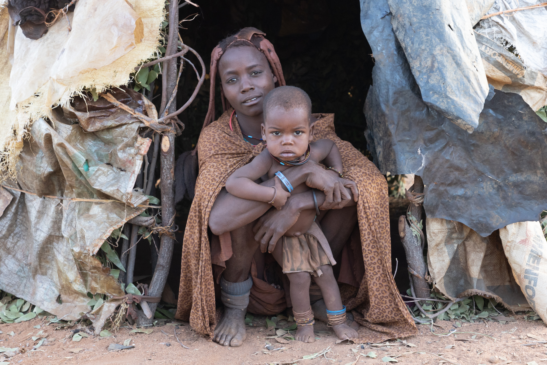 A Ovatwa mother holds her baby at the entrance of her home on our Angola tribal photography tour