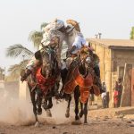 A pair of Batonu horsemen kiss as they race their horses through the street (image by Inger Vandyke)