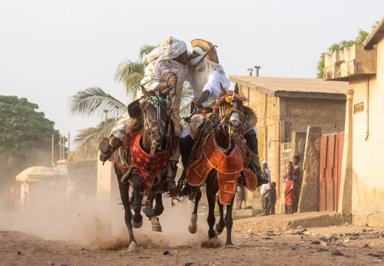 A pair of Batonu horsemen kiss as they race their horses through the street (image by Inger Vandyke)