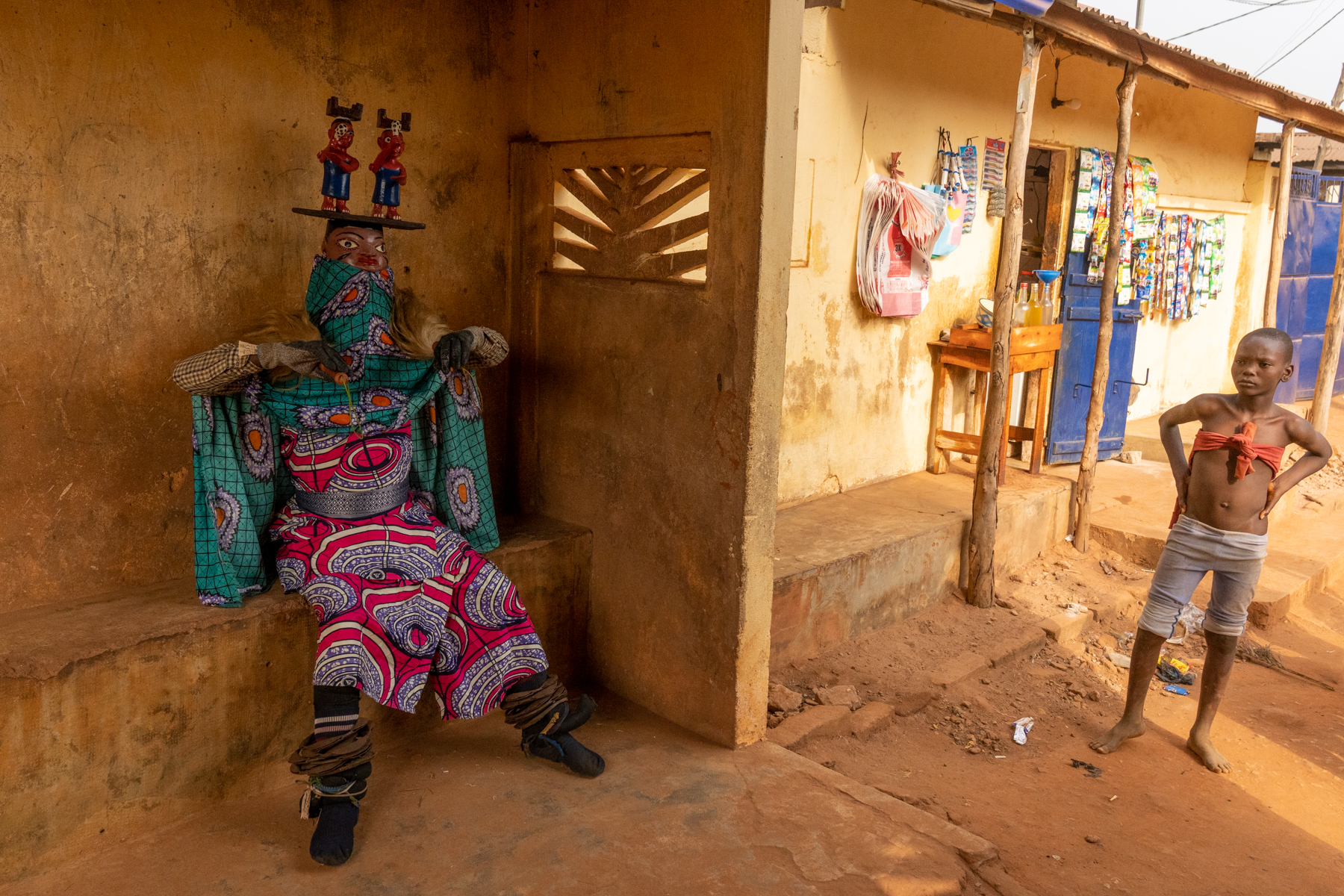 Street view of a Guèlèdè dancer with a curious local child (image by Inger Vandyke)