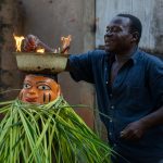 A Guèlèdè mask carver ignites the flaming bowl on the top of a dancer's head (image by Inger Vandyke)
