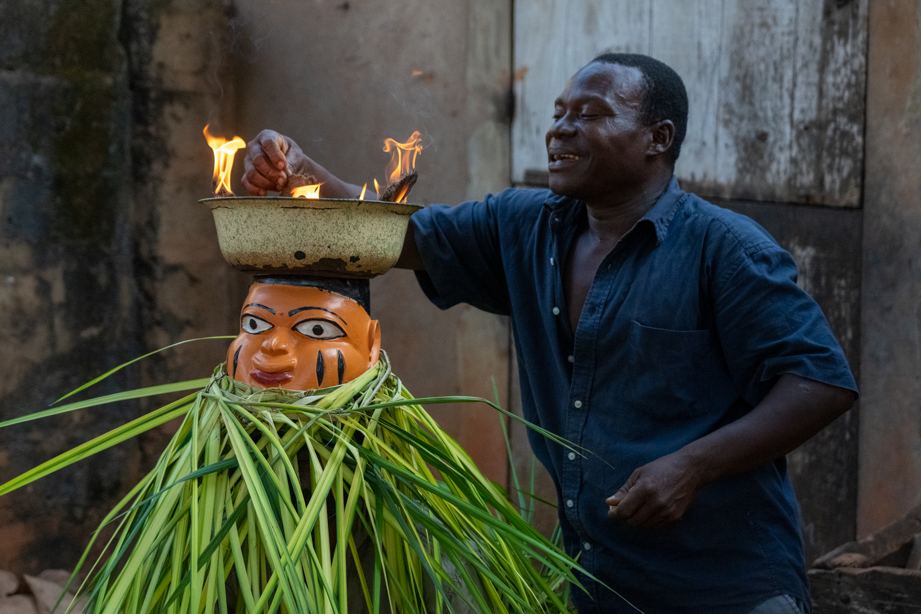 A Guèlèdè mask carver ignites the flaming bowl on the top of a dancer's head (image by Inger Vandyke)