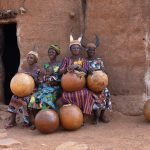 A group of Otamari women sit outside an ancient Tata house with their gigantic drums made from gourds (image by Inger Vandyke)