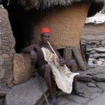 A Taneka spiritual healer of fertility sits outside his home smoking a long pipe (image by Inger Vandyke)