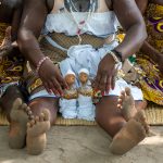 Looking after her twin babies, a Vodunsi woman sits watching her counterparts in a ceremony (image by Inger Vandyke)