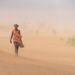 A Dassanech nomad woman braves a sudden sand storm to greet us on the side of the road (image by Inger Vandyke)