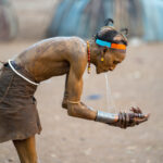 A Dassanech man cleans his hands of ochre using water from his mouth. This is a common way of preserving water in the nomadic people of Africa (image by Inger Vandyke)