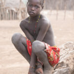 A shy young Karo girl watches us from the log she chose to sit on in her village (image by Inger Vandyke)