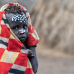 A young Mursi child stays warm at sunrise (image by Inger Vandyke)