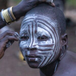 A friend runs her fingers through the chalk paint on a Mursi woman's face, to create decorative lines (image by Inger Vandyke)