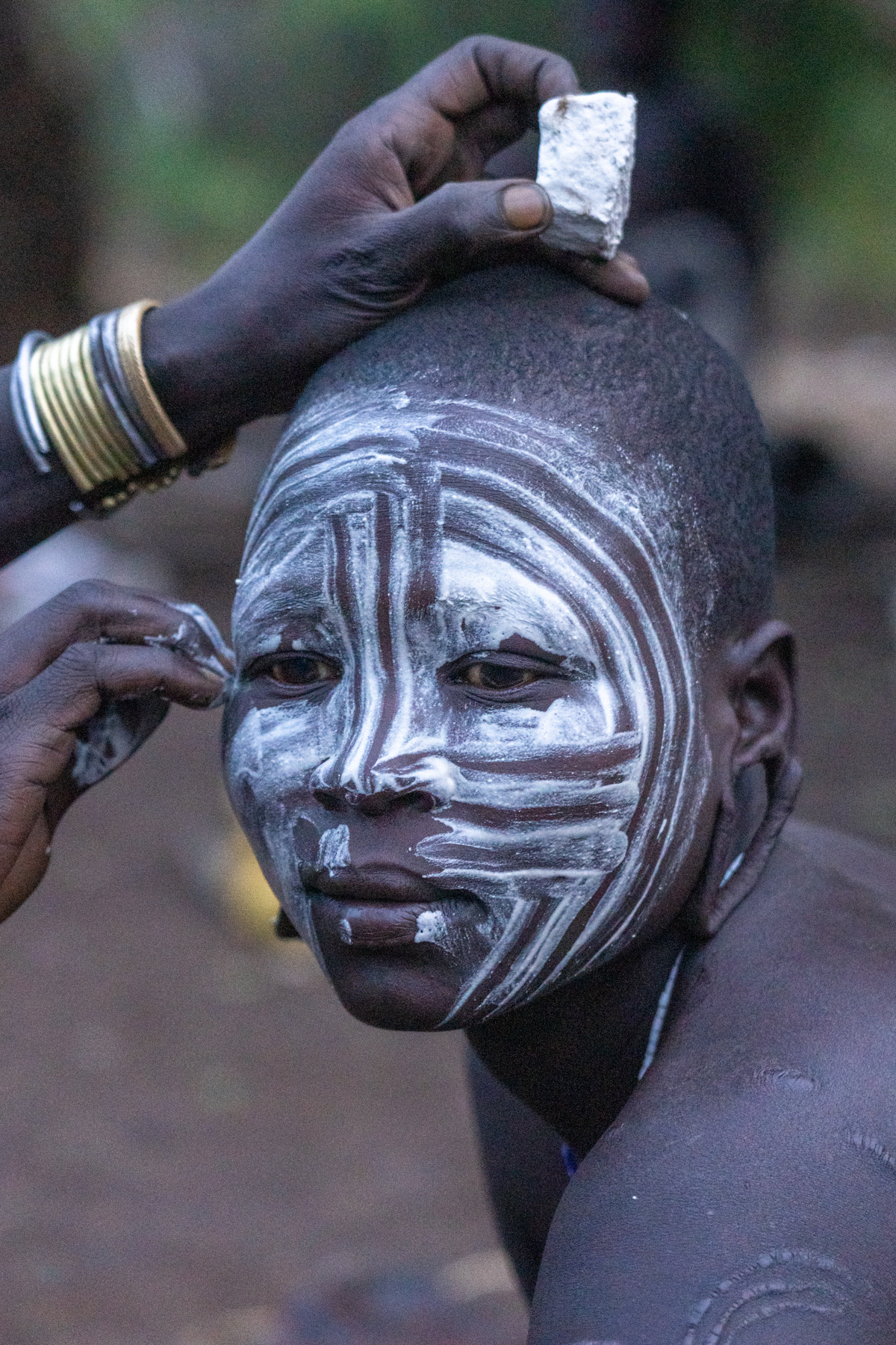 A friend runs her fingers through the chalk paint on a Mursi woman's face, to create decorative lines (image by Inger Vandyke)