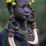 Portrait of a Mursi woman with her bush tomatoes, warthog tusks and heavy metal headdress (image by Inger Vandyke)