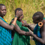 A female friend covers the eyes of her girlfriend undergoing scarification in Suri culture (image by Inger Vandyke)