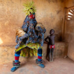 Guelede is all about all things women and children. Here a young child looks up at a Guelede masked dancer in admiration (image by Inger Vandyke)