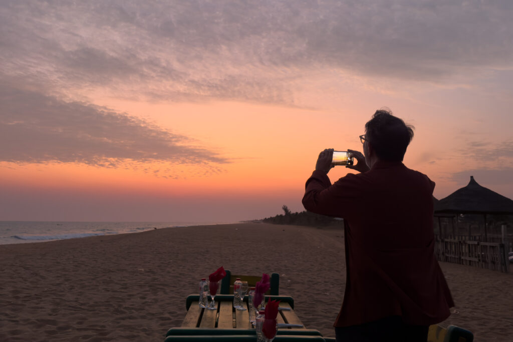 Guest David grabbing a quick iPhone snapshot of the stunning sunset on the beach, shortly before some local live musicians arrived to play Togolese Djembe for us while we ate delicious barbecued food (image by Inger Vandyke)