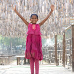 A young girl leaps into the air under fish drying racks (image by Inger Vandyke)