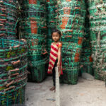 A young girl holds a fishing net in a sea of fish baskets (image by Inger Vandyke)