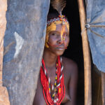 A painted Dassanech woman, dressed for Micha, in the doorway of her home (image by Inger Vandyke)