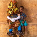 Guèlèdè dancer wearing a mask depicting cooking posing with a young boy (image by Ingrid Koedood)