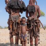 An Ovahimba girl holding the skirts of her mother and sister (image by Inger Vandyke)